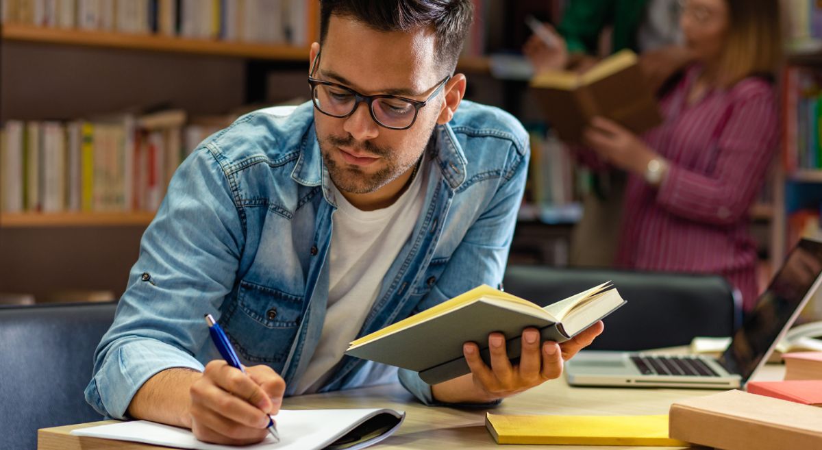 Stock picture showing an adult holding a book and writing in a Library